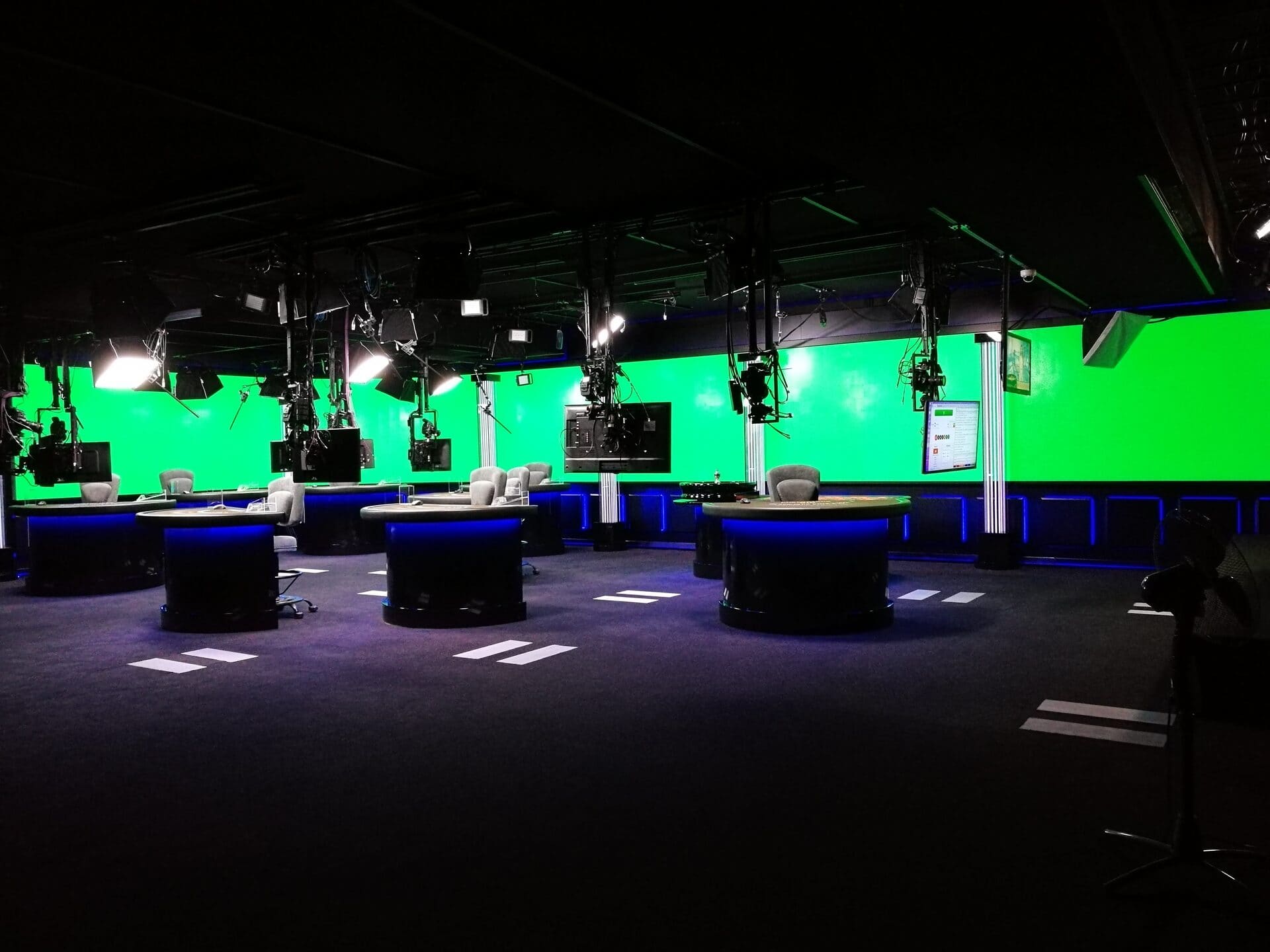 Студия трансляций live-казино: игровые столы на подиумах с LED-подсветкой, камеры на потолочных фермах и хромакей